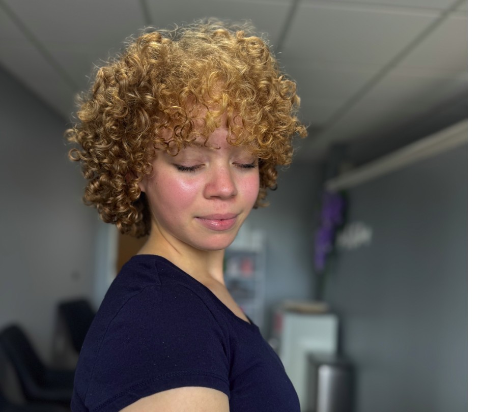 Guest with a rounded, defined curly cut in a honey blonde shade