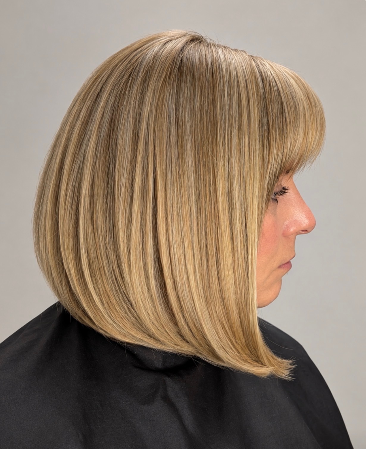 Dimensional blonde highlights and a precisely shaped bob with side-swept bangs at DLuxe Beauty Consulting