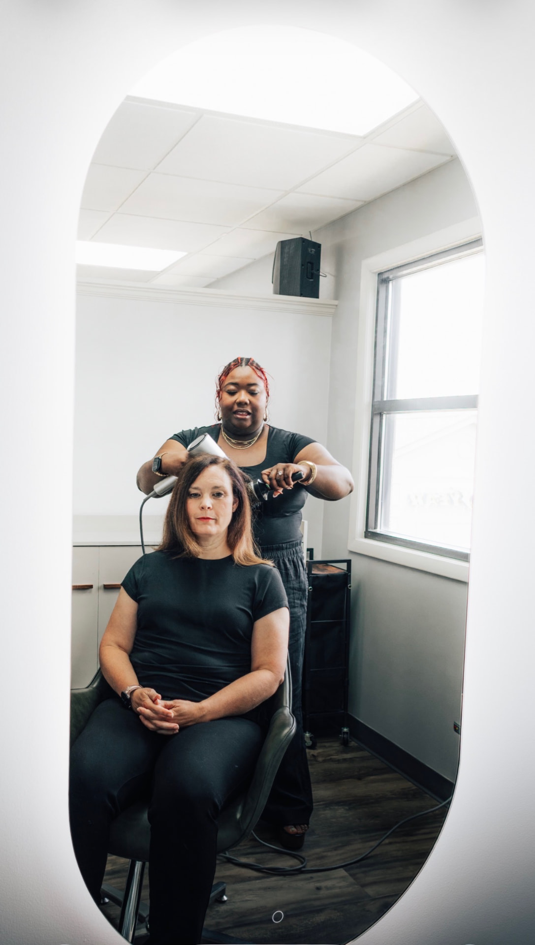 Danis styling a client's hair at DLuxe Beauty Consulting, reflected in the salon mirror